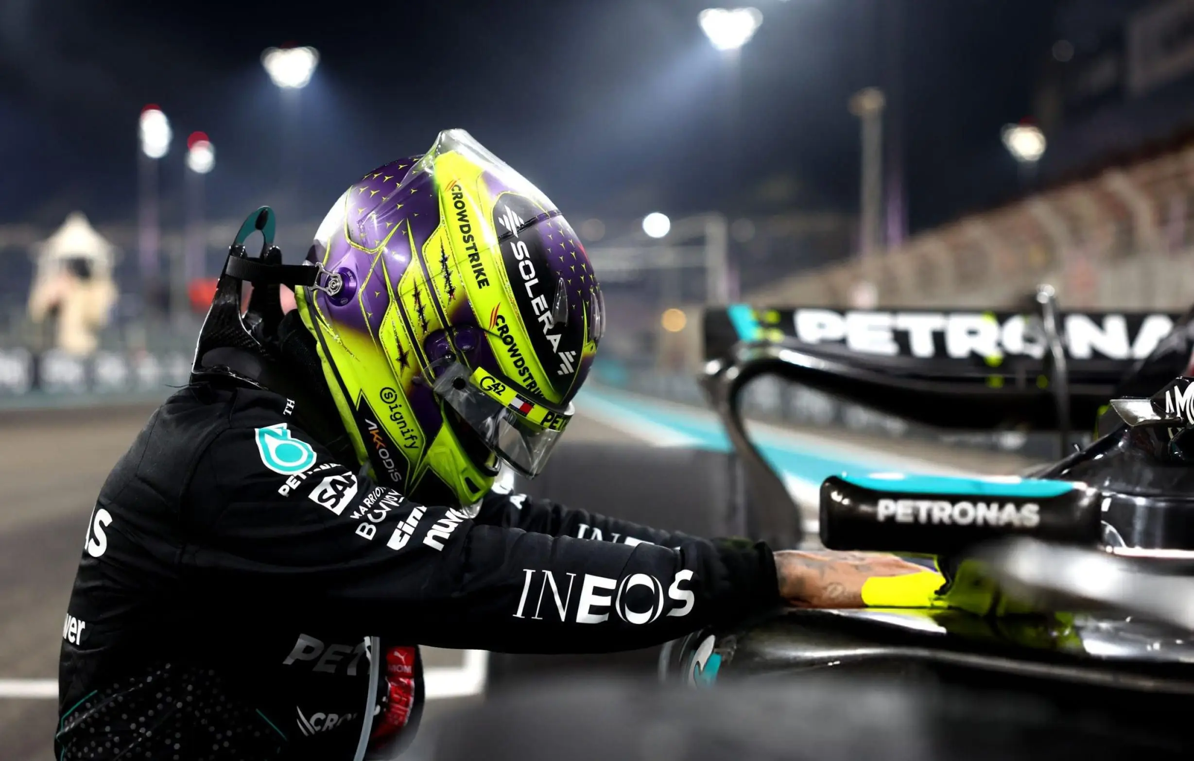 Driver in a Mercedes race suit leaning over the cockpit, helmet catching the light